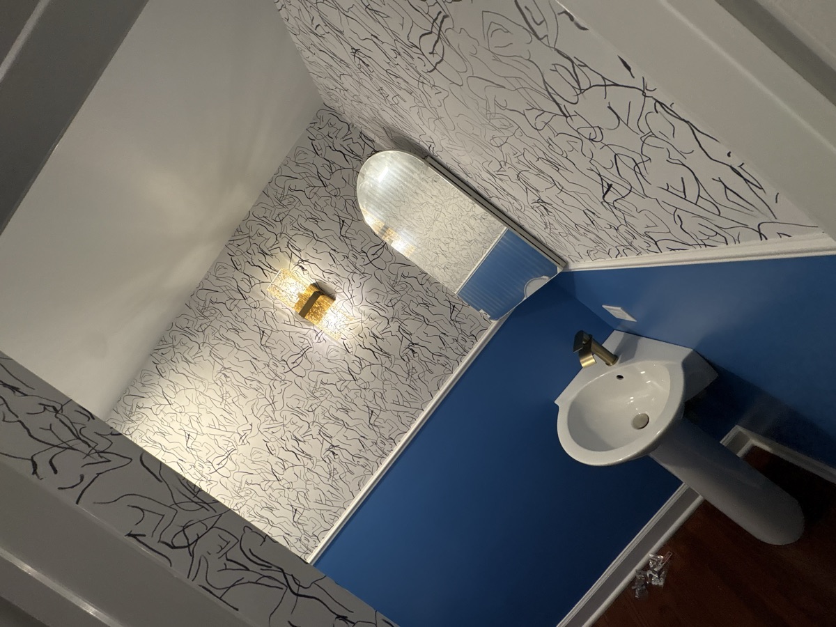 Powder room with designer wallpaper, blue accent wall, and gold fixtures