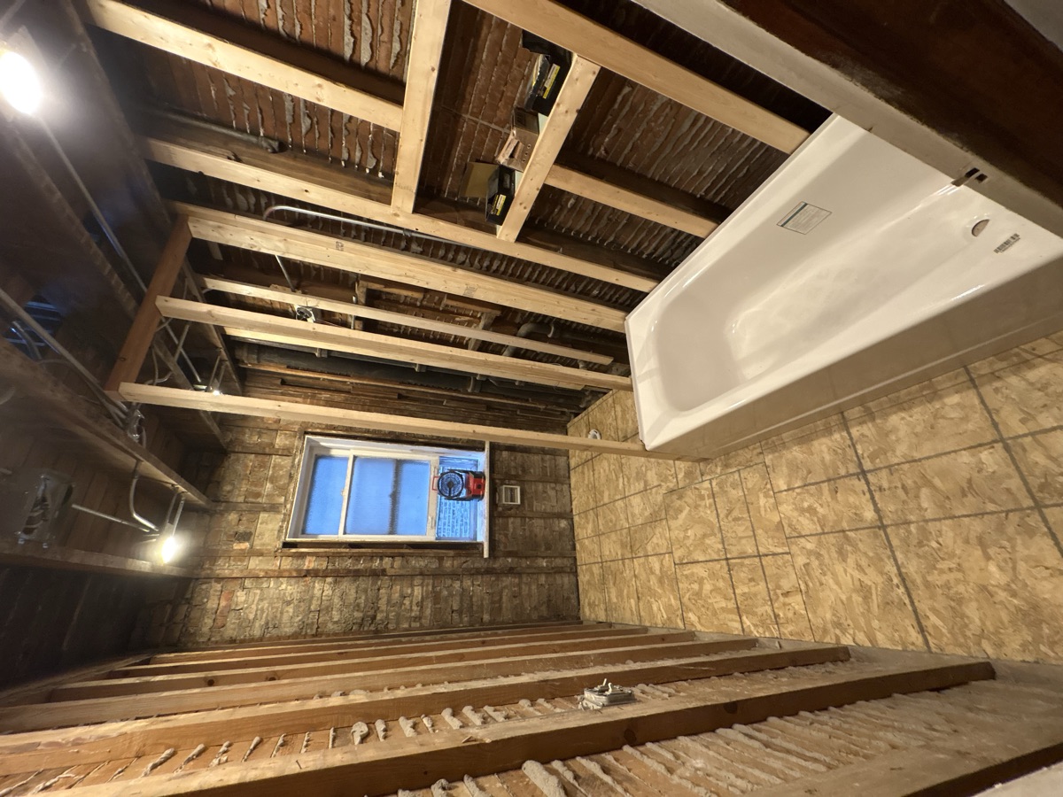 Bathroom before remodel - exposed framing, bathtub, and subfloor